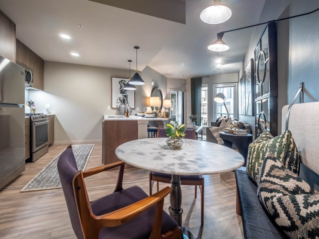 Furnished open concept apartment with a parallel style kitchen, dining area, and living room featuring wood flooring, stainless steel appliances, and pendant, recessed and track lighting.