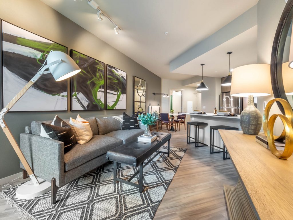 Furnished apartment living room and kitchen with wood floors, counter with barstool seating, and track and pendant lighting.