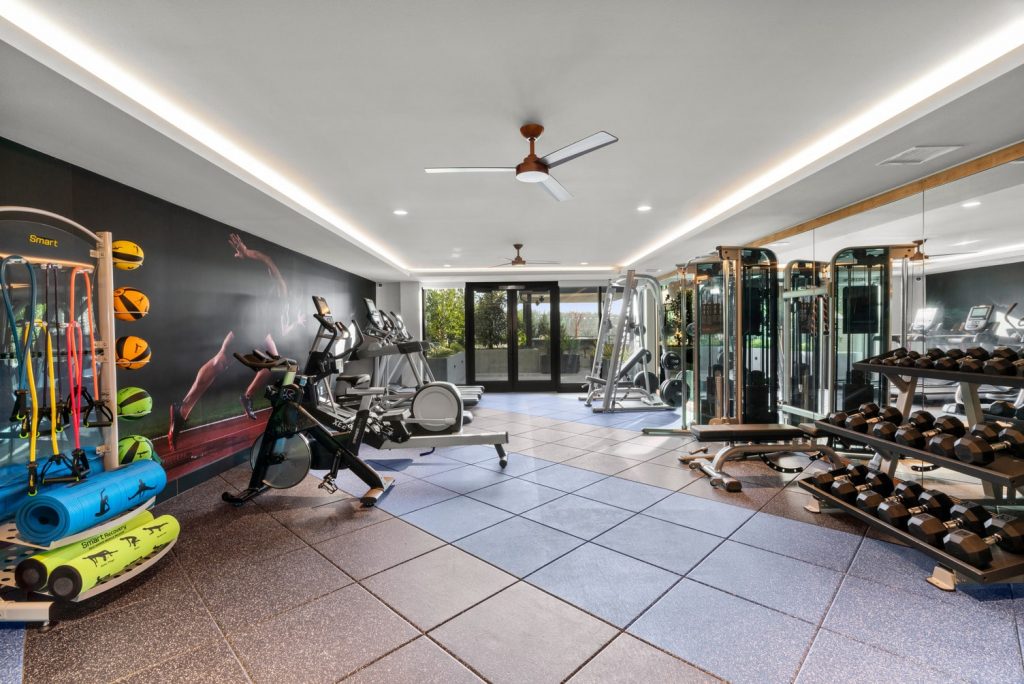 Fitness center with treadmills, ellipticals, various weight machines, free weights, yoga mats, medicine balls, a large floor-to-ceiling wall mirror opposite of a wall mural.