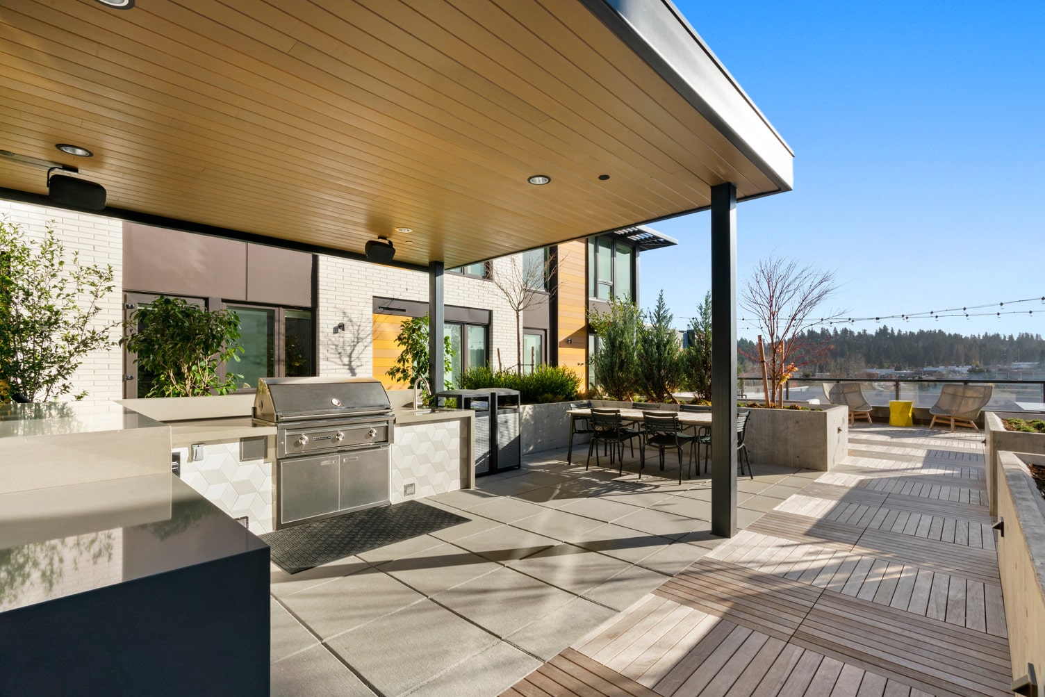 Covered outdoor grill area with dining table, raised planters, and string lighting.