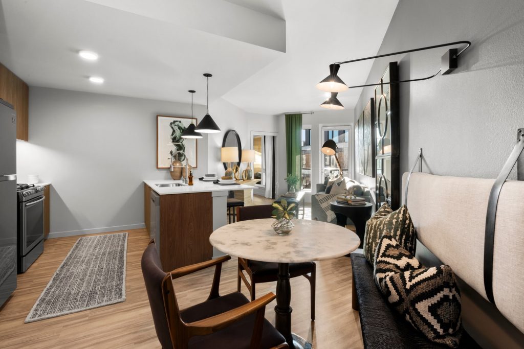 Furnished apartment living room, dining room and kitchen with a peninsula counter with an overhang for bar stools, wood flooring, and hanging lights.