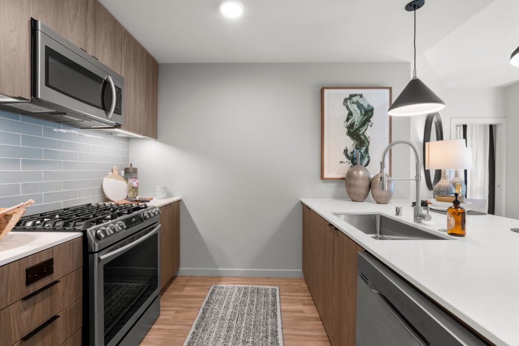 Apartment parallel style kitchen with wood flooring, stainless steel appliances, a gas stovetop, under-mounted single basin sink, tile backsplash, and hanging and recessed lighting.