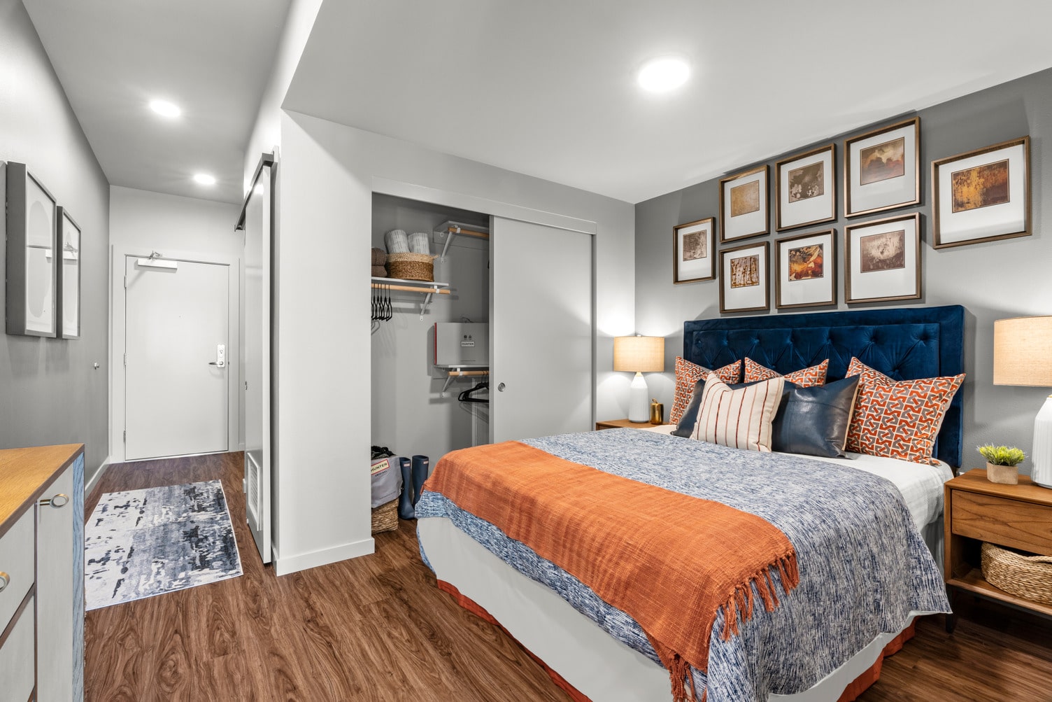 Furnished studio apartment bedroom area with wood flooring, sliding barn style door, and a closet.